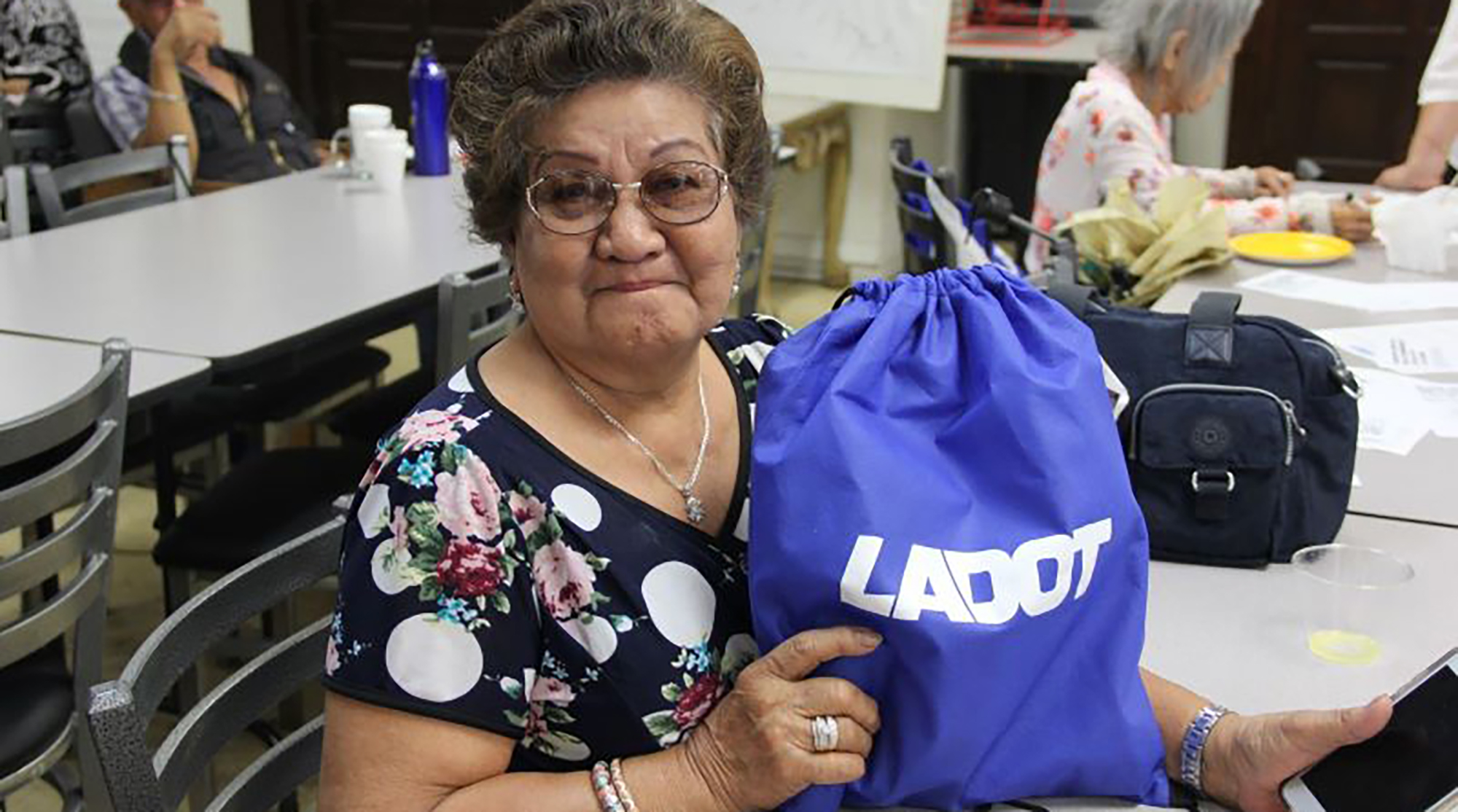 A female senior is holding an blue bag with LADOT logo for Safe Routes for Seniors